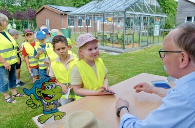 Bürgermeister Dr. Tobias Lehberg drückt, assistiert vom Energietroll Energix, im Energiewelten-Garten im Bioenergiepark den letzten Stempel in die Laufkarten der Kita-Vorschulkinder, die dann ihren "Forscherpass für Klimaschützer" nach vier Lern- und Erlebnismodulen komplett haben.
