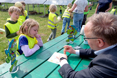 Bürgermeister Dr. Tobias Lehberg drückt, assistiert vom Energietroll Energix, im Energiewelten-Garten im Bioenergiepark den letzten Stempel in die Laufkarten der Kita-Vorschulkinder, die dann ihren &quot;Forscherpass für Klimaschützer&quot; nach vier Lern- und Erlebnismodulen komplett haben.