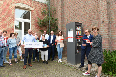 Mit Schwung lösen Initiatoren, Unterstützer und Förderer die Schleife um den Offenen Bücherschrank auf dem Dorfplatz und geben das neue Angebot frei für alle, die gerne lesen und Bücher teilen.