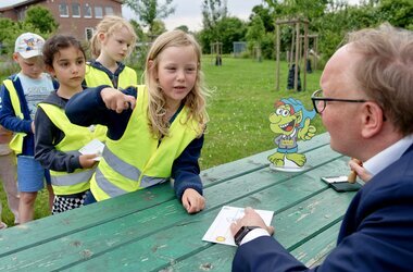 Bürgermeister Dr. Tobias Lehberg drückt, assistiert vom Energietroll Energix, im Energiewelten-Garten im Bioenergiepark den letzten Stempel in die Laufkarten der Kita-Vorschulkinder, die dann ihren "Forscherpass für Klimaschützer" nach vier Lern- und Erlebnismodulen komplett haben.